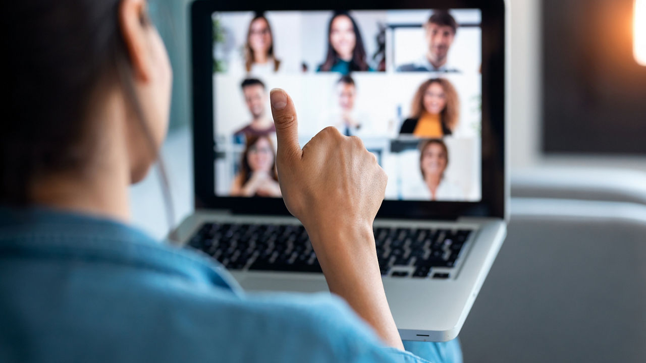 Back view of business woman making video call and showing thumb up to laptop on the online briefing while sit on sofa at home