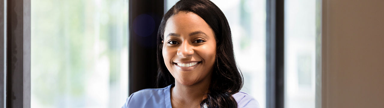 An attractive mid adult female nurse stands with her arms crossed in the hospital corridor