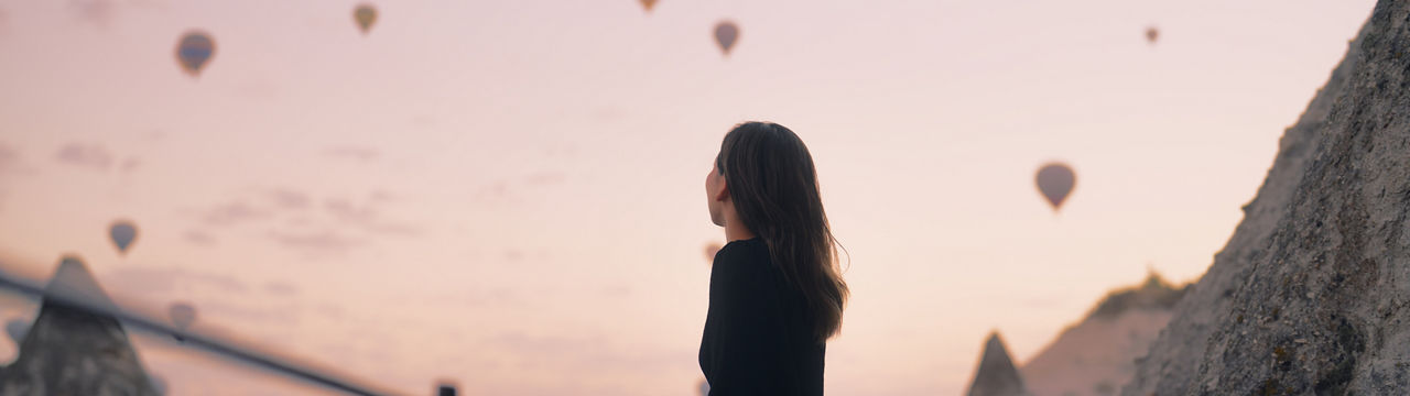 A female tourist is enjoying watching hot air balloons flying in the sky at the rooftop of the hotel where she is staying during her vacation.