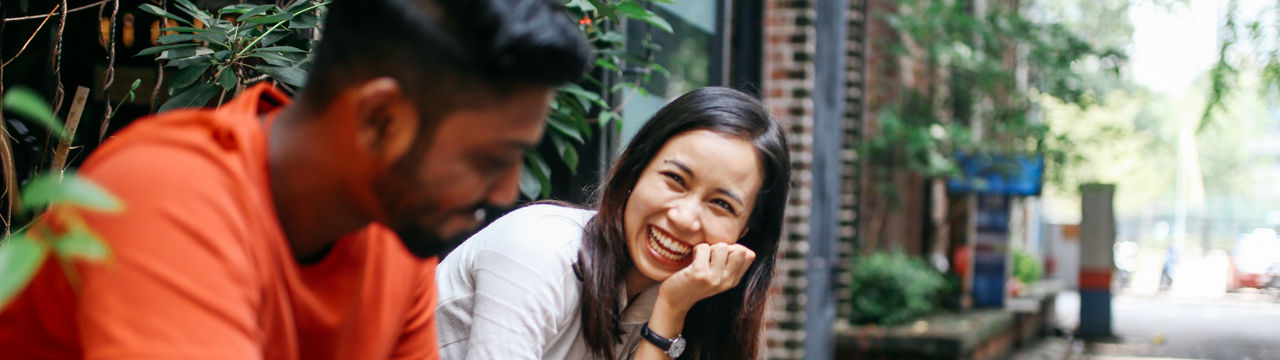 Young people talking and flirting on the streets of Kuala Lumpur, having a coffee break together in front of their office or university library.