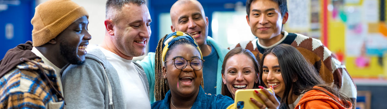 Waist-up shot of friends taking a selfie together in a community centre. They are being silly for the camera all wearing casual clothing. The community centre is in Seaton Deleval in the North East of England.