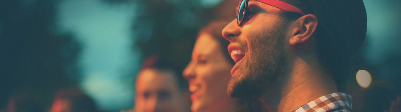 Group of people clapping and cheering after music performance. Standing side by side. There are two guys and one girl and large crowd behind.The closest guy is in focus.Side view.