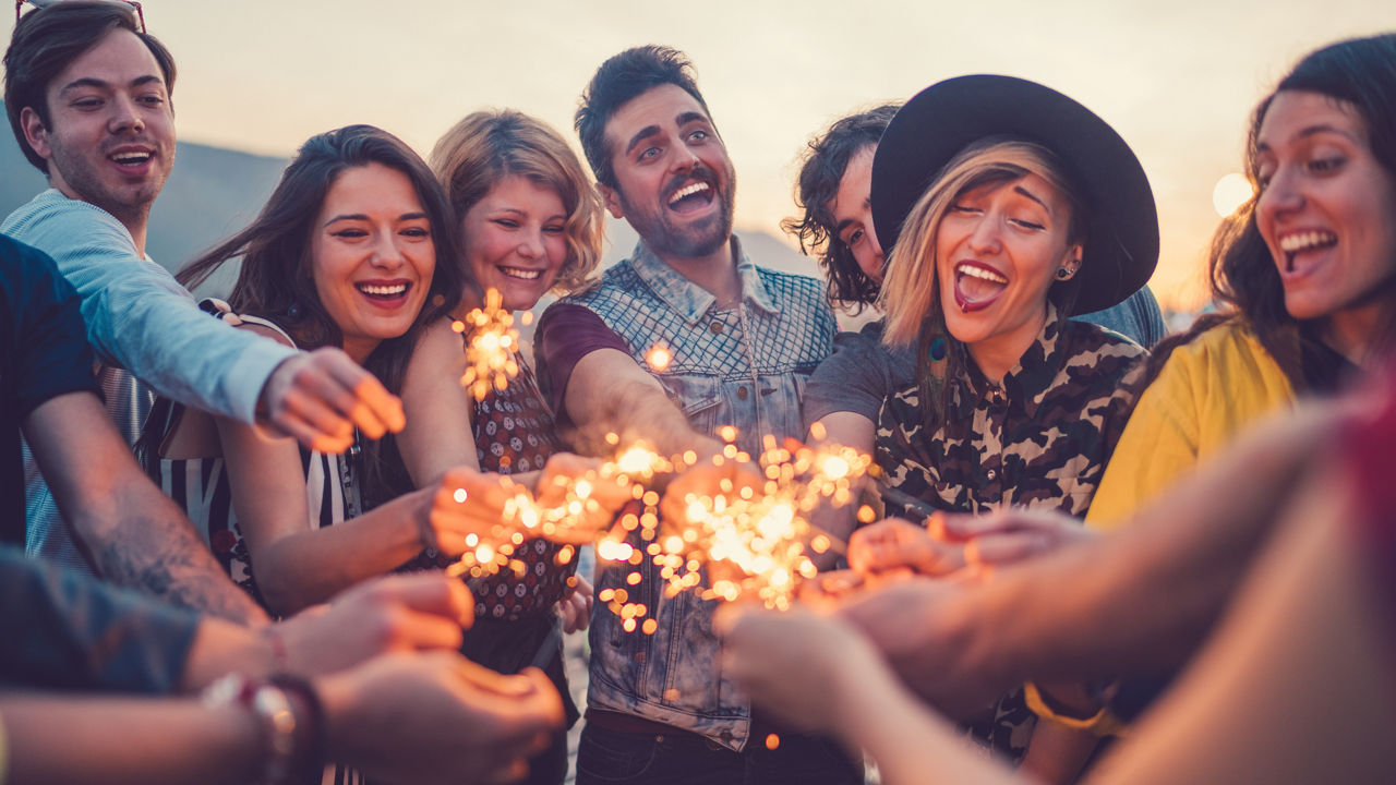 Happy friends holding burning sparklers on rooftop party