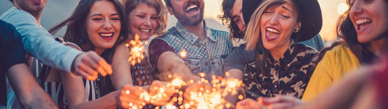 Happy friends holding burning sparklers on rooftop party