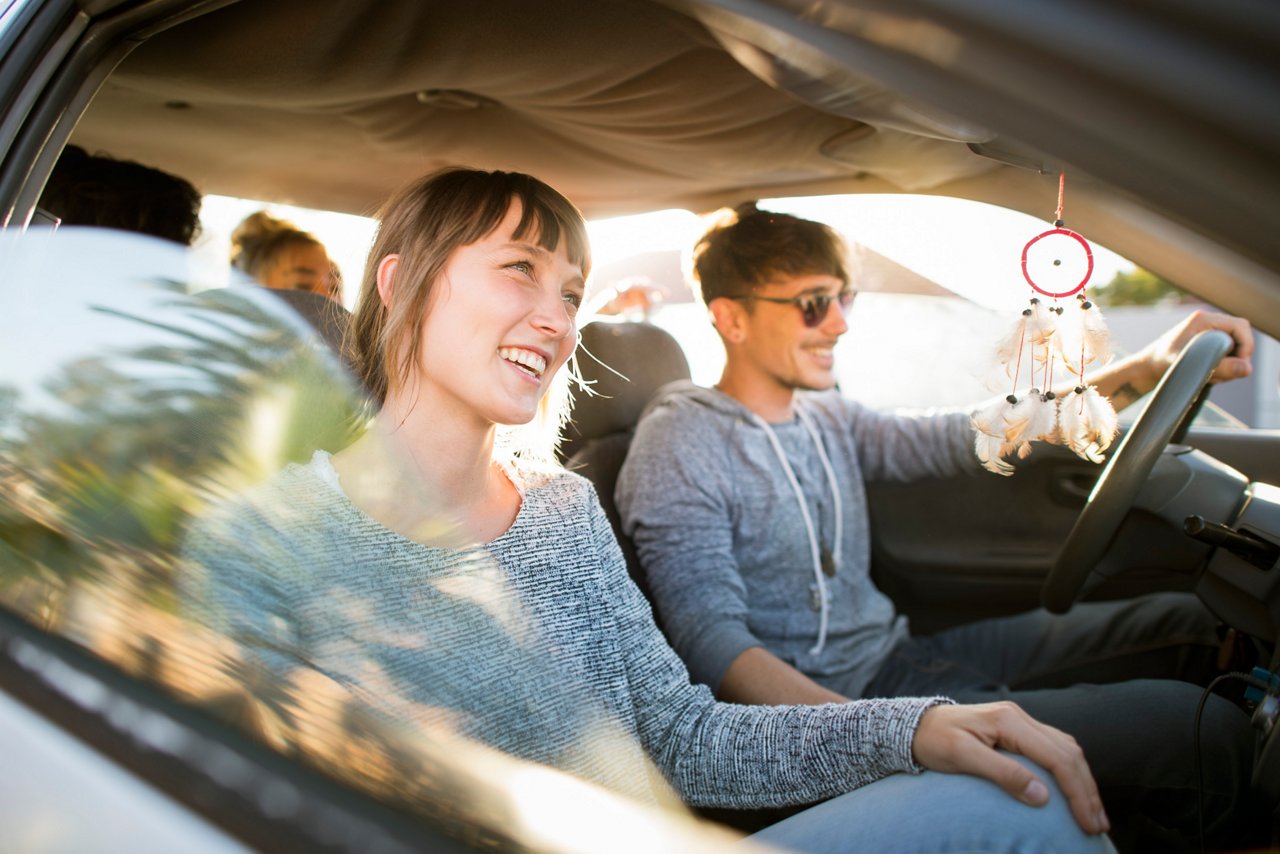 Smiling men and women traveling in car. Young friends are enjoying in road trip. They are wearing casuals during summer vacation.