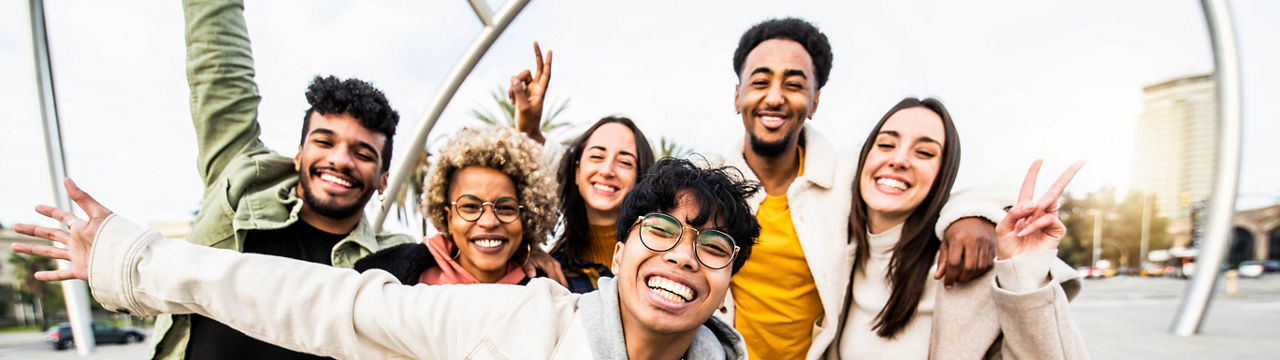 Big group of happy friends stands together on city street with raised arms - Multiracial young people having fun outside - Volunteer with hands up showing teamwork spirit - Community and friendship