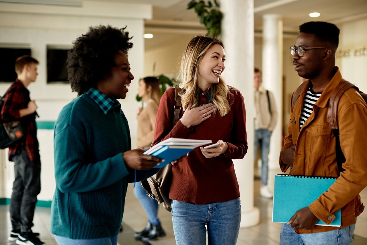 Happy students having fun while communicating at university hallway.