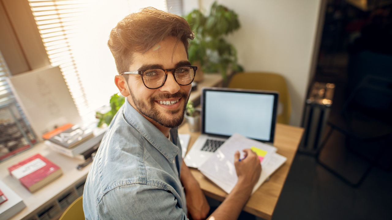 Portrait of happy motivated smiling hipster student learning for a test or an exam at high school library desk while sitting turn backwards and looking at the camera