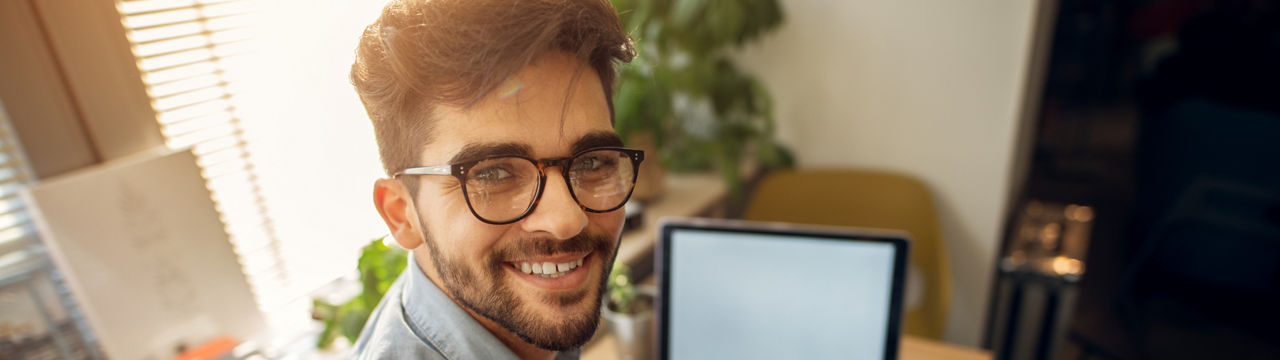 Portrait of happy motivated smiling hipster student learning for a test or an exam at high school library desk while sitting turn backwards and looking at the camera