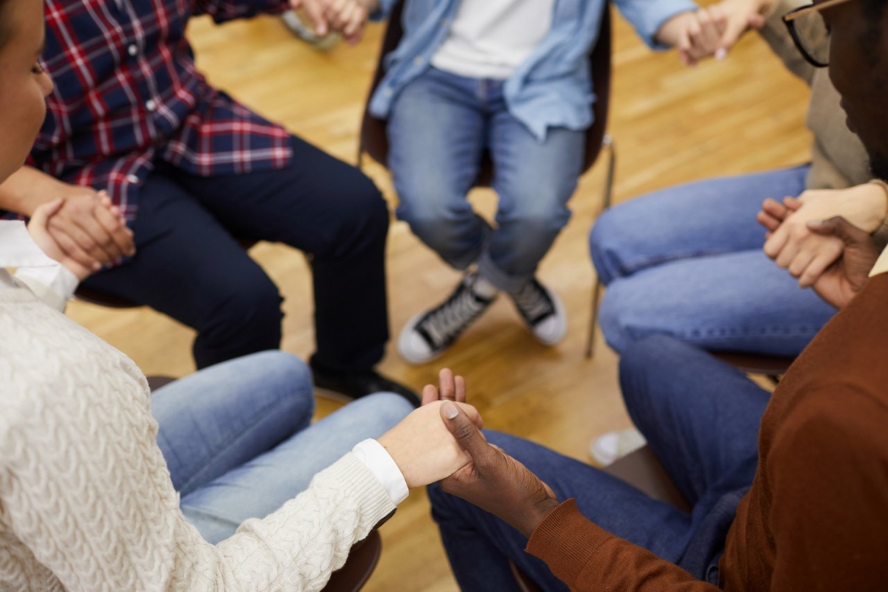 High angle closeup of unrecognizable people sitting in circle and holding hands during support group meeting