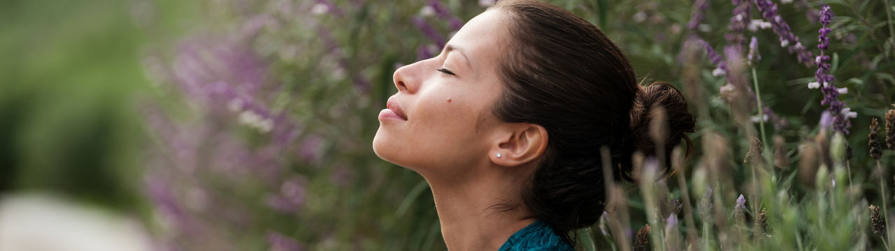 A latin woman sitting with her eyes closed and relaxing next to some flowers.