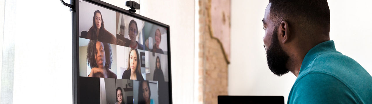 A mid adult man gestures while talking with a group of colleagues during a virtual staff meeting via video conference