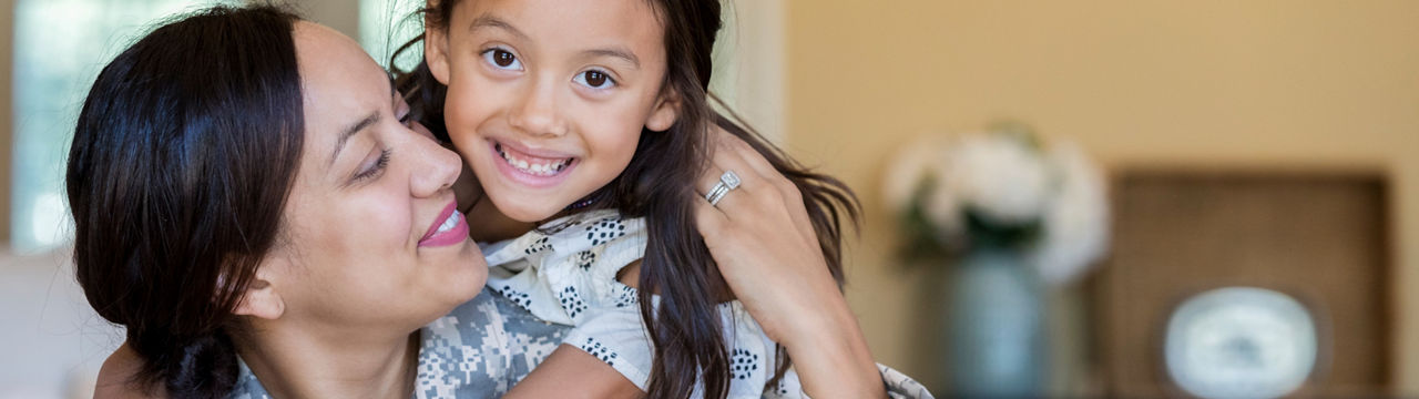 Little girl rides piggyback on her mom's back. Her mom has just returned from military assignment 