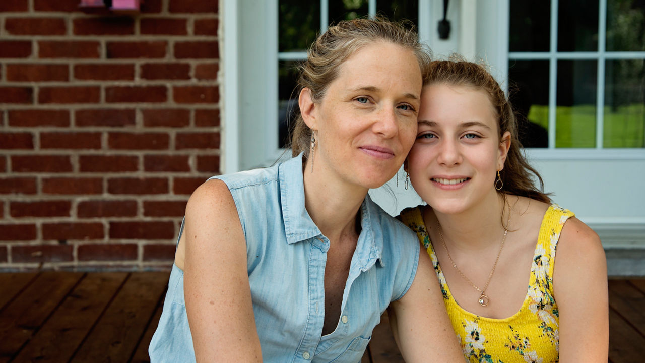 Real family portrait of mother and teenage daughter on home porch in summer. Mom is in her forties, girl is 12 yearâ  s old. Everybody is casually dressed for summer. Horizontal waist up outdoors shot with copy space.