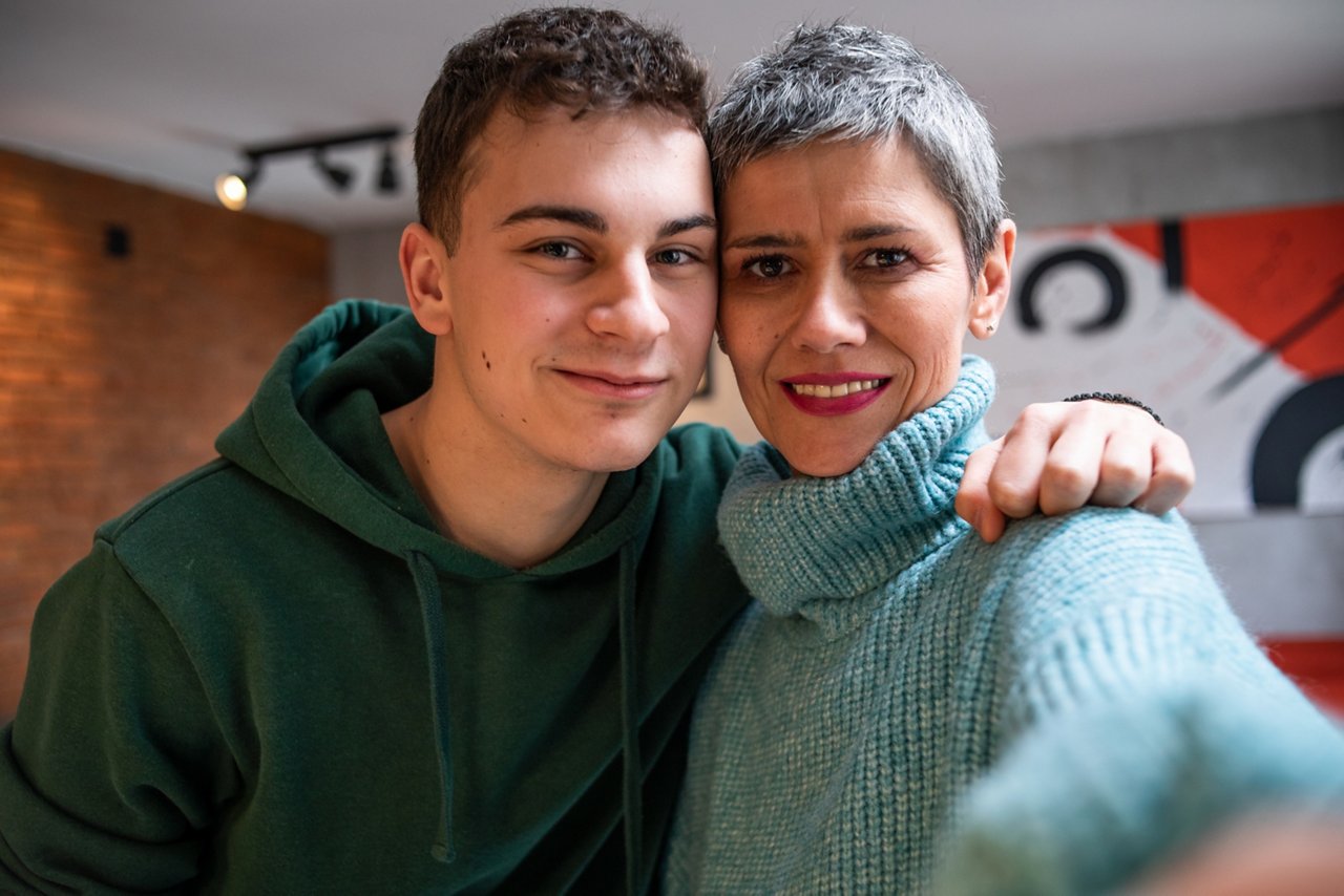 Mother and teenage son hugging, having fun and looking at mobile phone, taking selfie