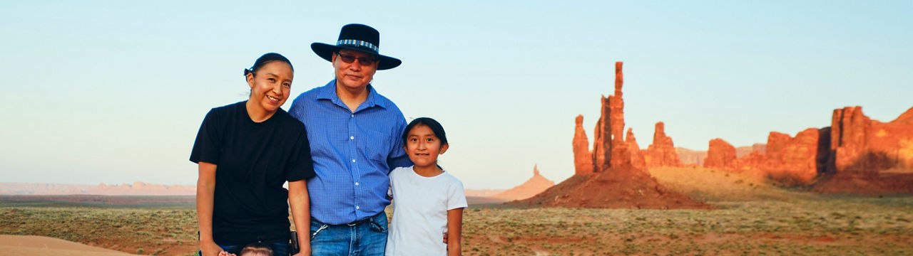 A Navajo family standing on the sand in Monument Valley at sunset.