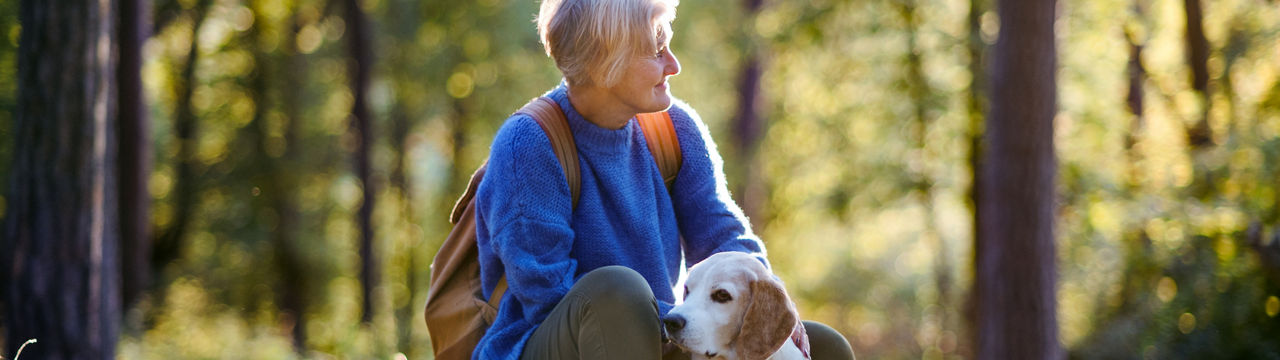 A happy senior woman with dog on a walk outdoors in forest