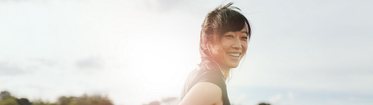 Outdoor shot of smiling young woman runner looking at camera. Chinese female walking on field in morning