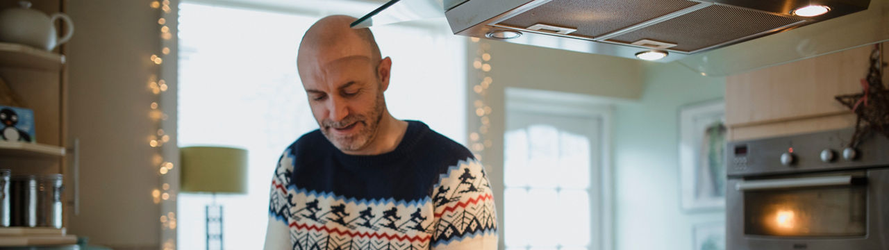 One mature man is preparing a christmas dinner in the kitchen of his home. He is peeling carrots and parsnips.