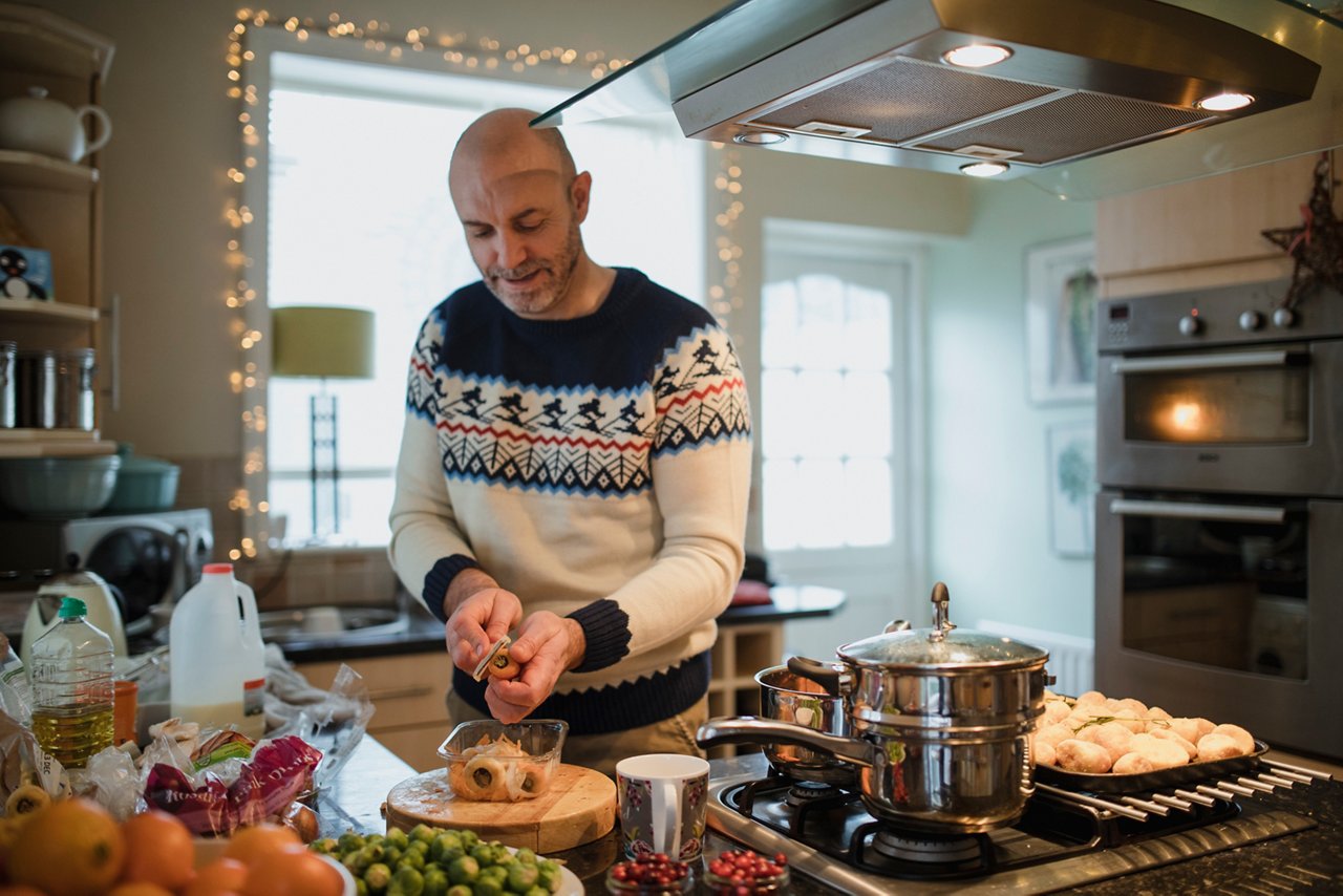 One mature man is preparing a christmas dinner in the kitchen of his home. He is peeling carrots and parsnips.