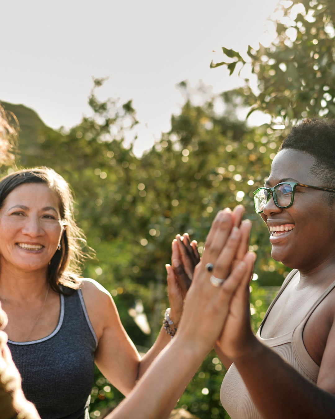 Laughing woman and a group of other women standing with her hands together during an exercise at a wellness retreat in summer