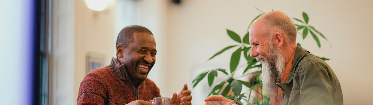 Two senior men are relaxing in a modern cafe, laughing and talking while enjoying green tea