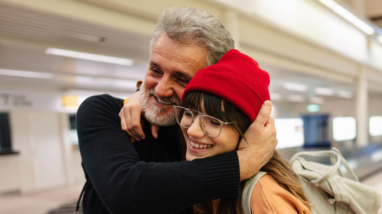 Photo of a young woman and her senior father meeting at the airport after a long time, reuniting after pandemic separations and isolation.