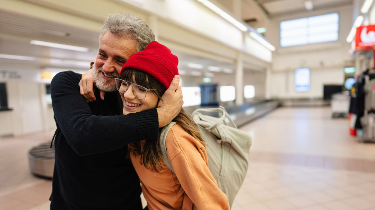 Photo of a young woman and her senior father meeting at the airport after a long time, reuniting after pandemic separations and isolation.