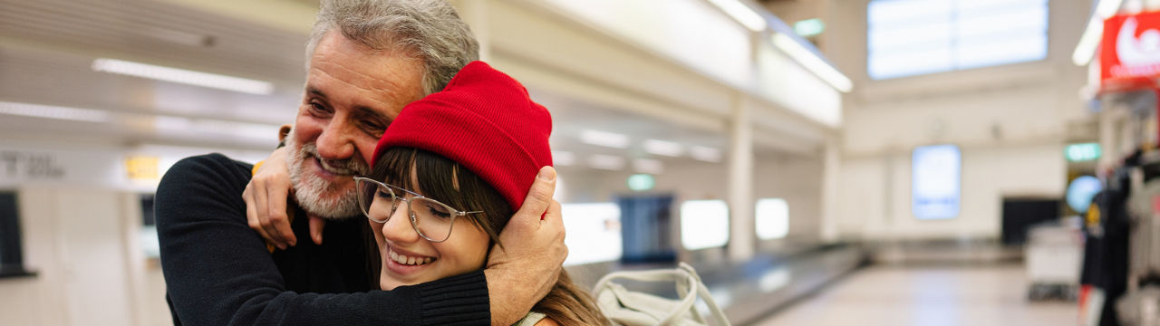 Photo of a young woman and her senior father meeting at the airport after a long time, reuniting after pandemic separations and isolation.