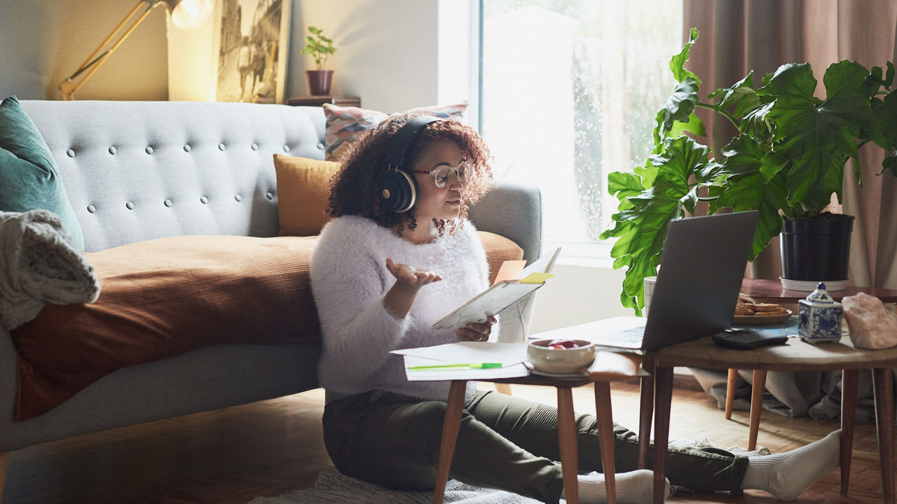 Shot of a young woman holding a notebook while making a video call on a laptop at home