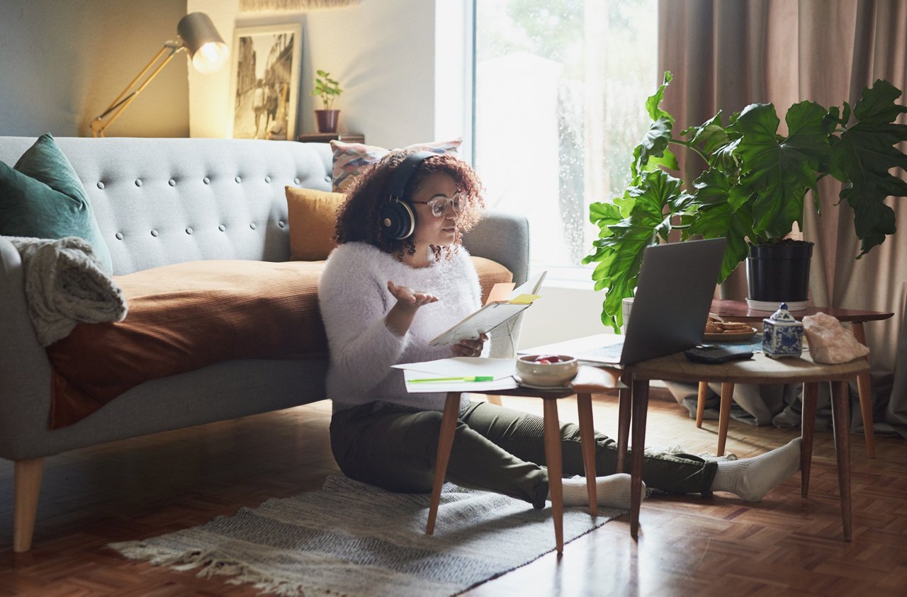 Shot of a young woman holding a notebook while making a video call on a laptop at home