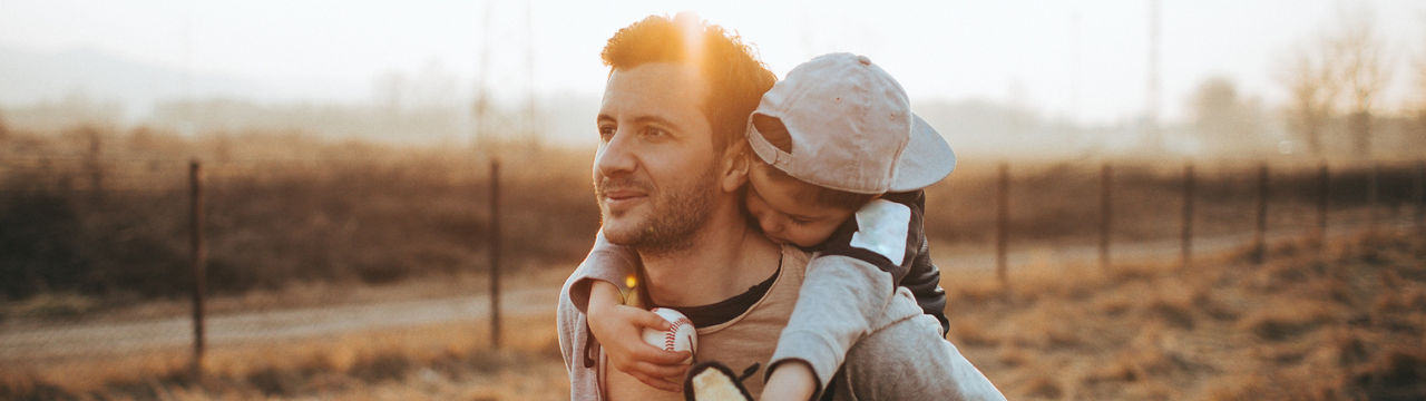 Photo of young father holding his son, tired baseball player after the training is over