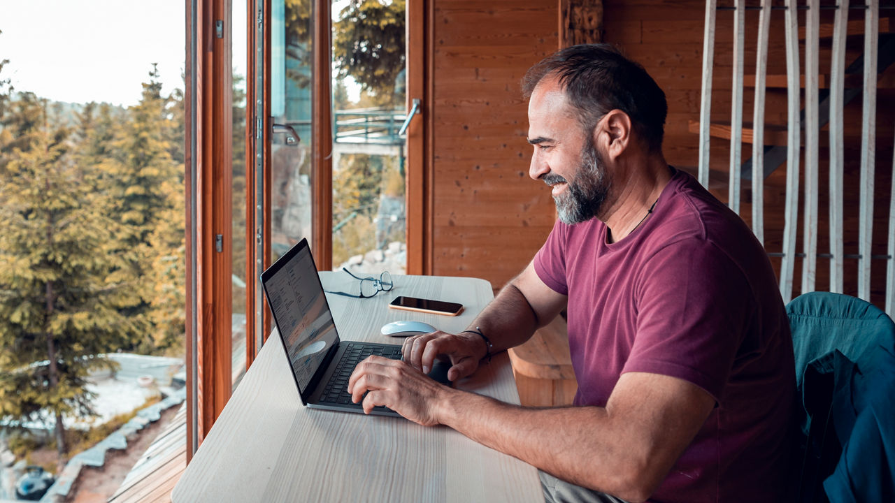 Close up of a mid adult man working on a laptop from his cabin in the woods