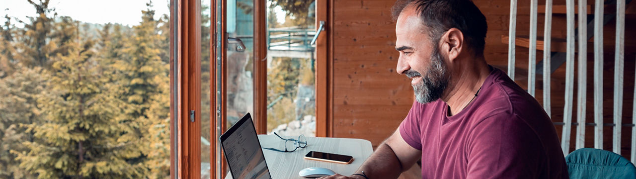 Close up of a mid adult man working on a laptop from his cabin in the woods