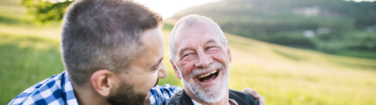 An adult hipster son with his senior father in wheelchair on a walk on a meadow in nature at sunset, laughing. Close up,man, men, male, dad, father, son, kid, child, pop, outdoors, field, laughter, laughing, fun, smile, smiling, friends, buddies, buddy, wheelchair, chair, hip, hipster, adult, senior, older adult, elder, happy, love, support, caring, happiness, joy, horizontal, disability, disabled, sunshine, nature, relationship, walk, meadow, sunset