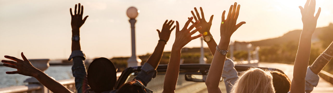 Group riding in open convertible hands up