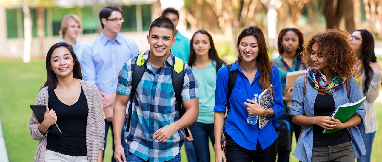 Banner size photo of diverse teenagers or young adults walking outdoors on school campus. 
