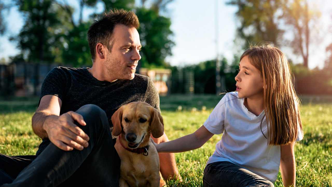 Father and daughter relaxing at park with small yellow dog