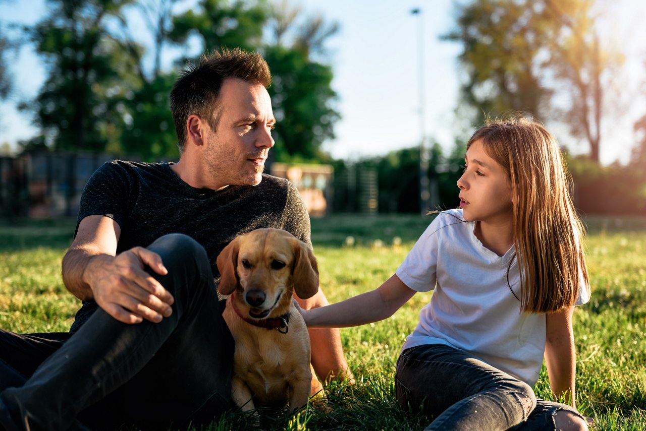 Father and daughter relaxing at park with small yellow dog