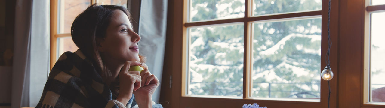 Portrait of redhead girl in plaid with apple sitting at table in kitchen