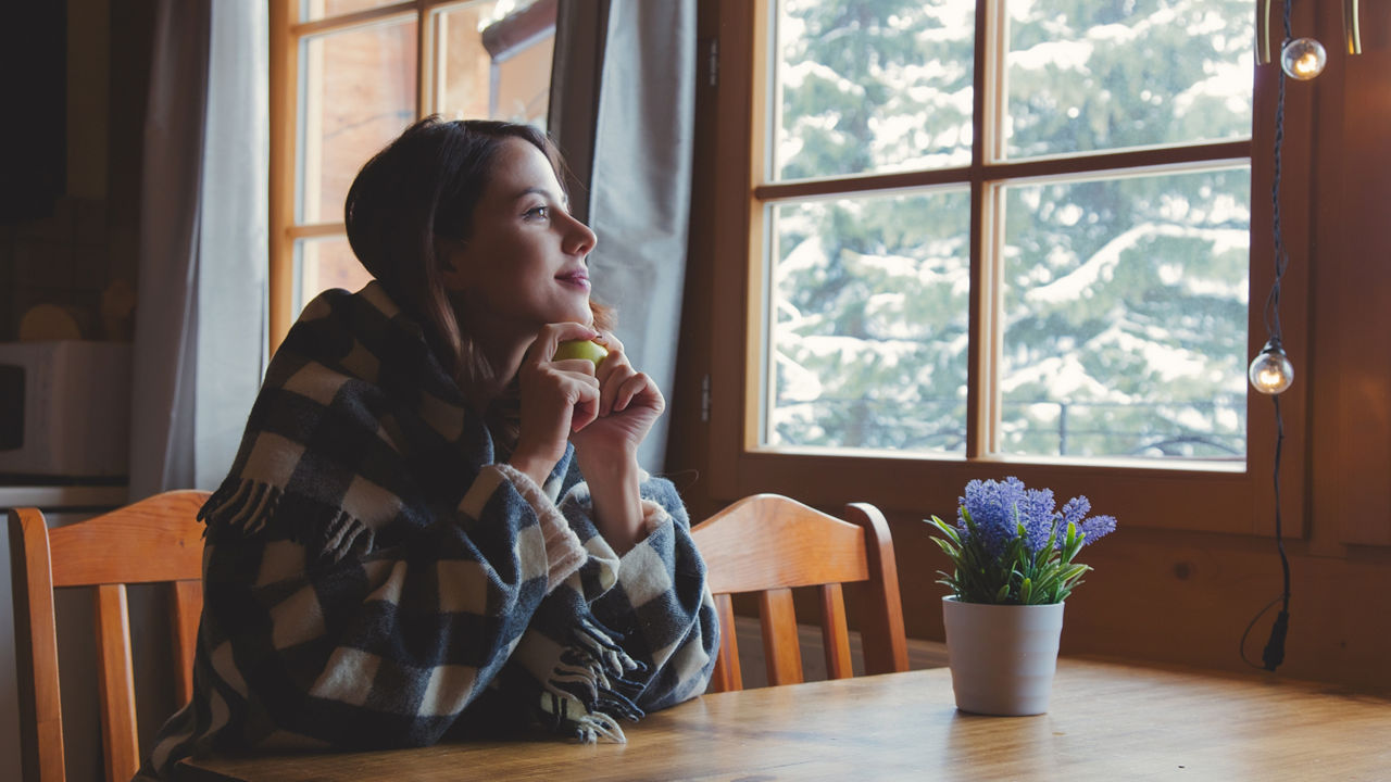 Portrait of redhead girl in plaid with apple sitting at table in kitchen