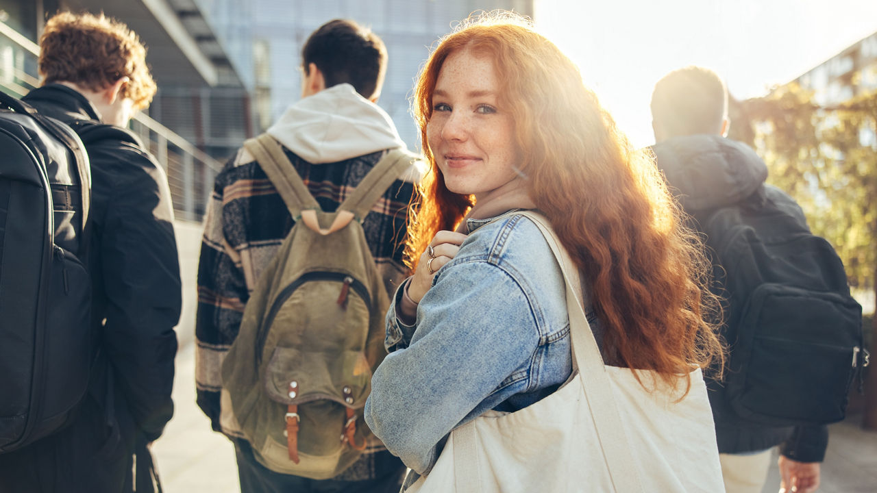 Female student glancing back while going for a class in college. Girl walking with friends going for class in high school