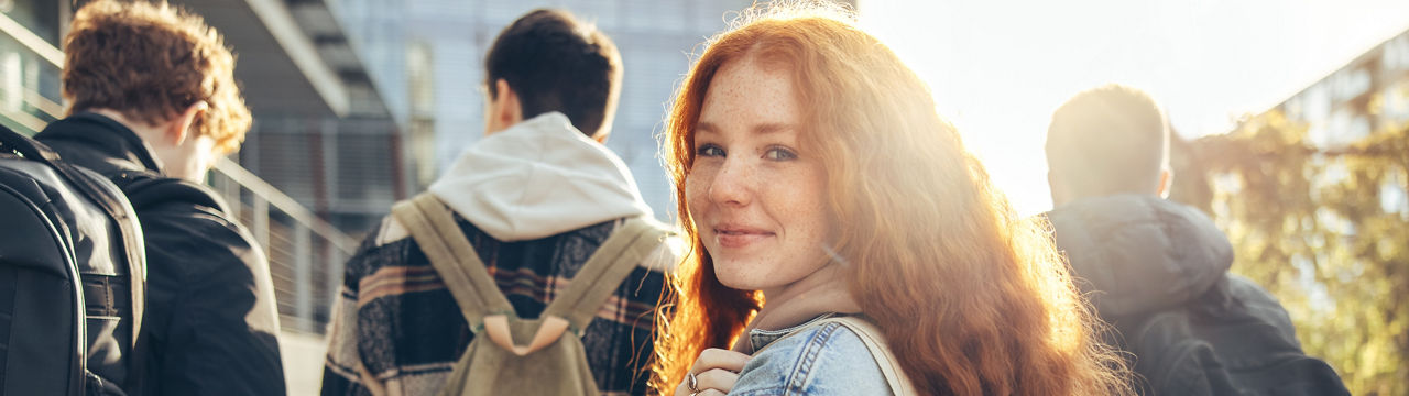 Female student glancing back while going for a class in college. Girl walking with friends going for class in high school