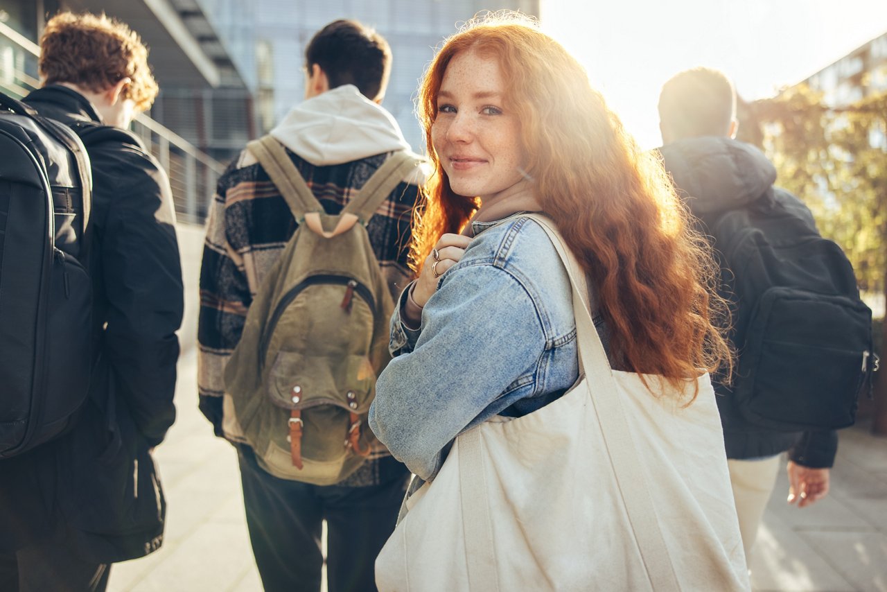 Female student glancing back while going for a class in college. Girl walking with friends going for class in high school