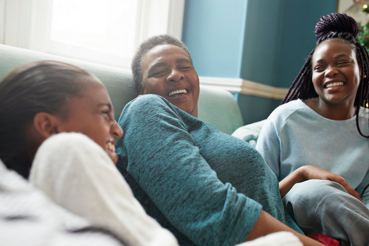 Grandmother laughing with granddaughters on sofa