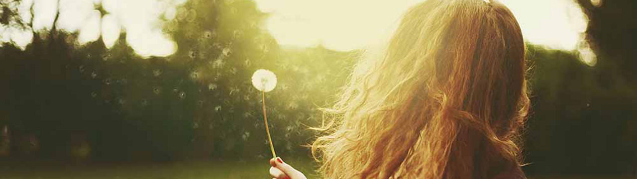 Female holding dandelion in wind for detachment