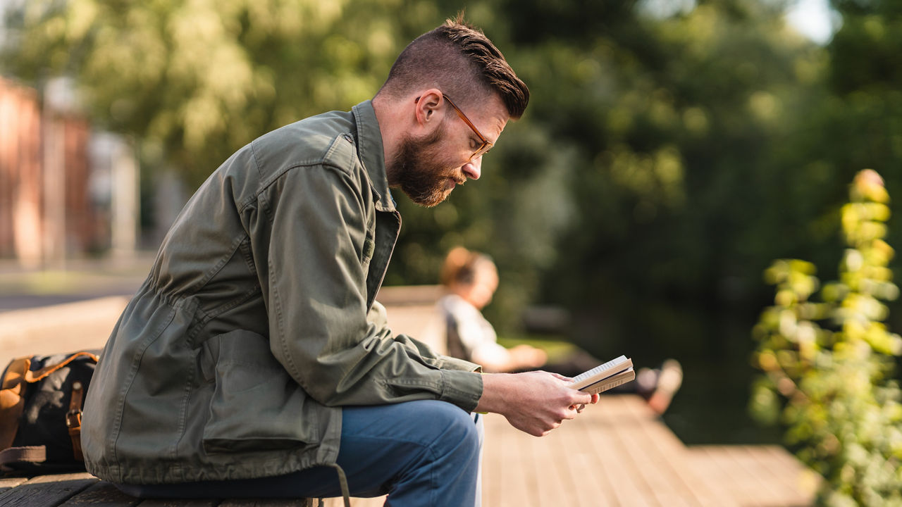 Man reading a paperback book in a public park