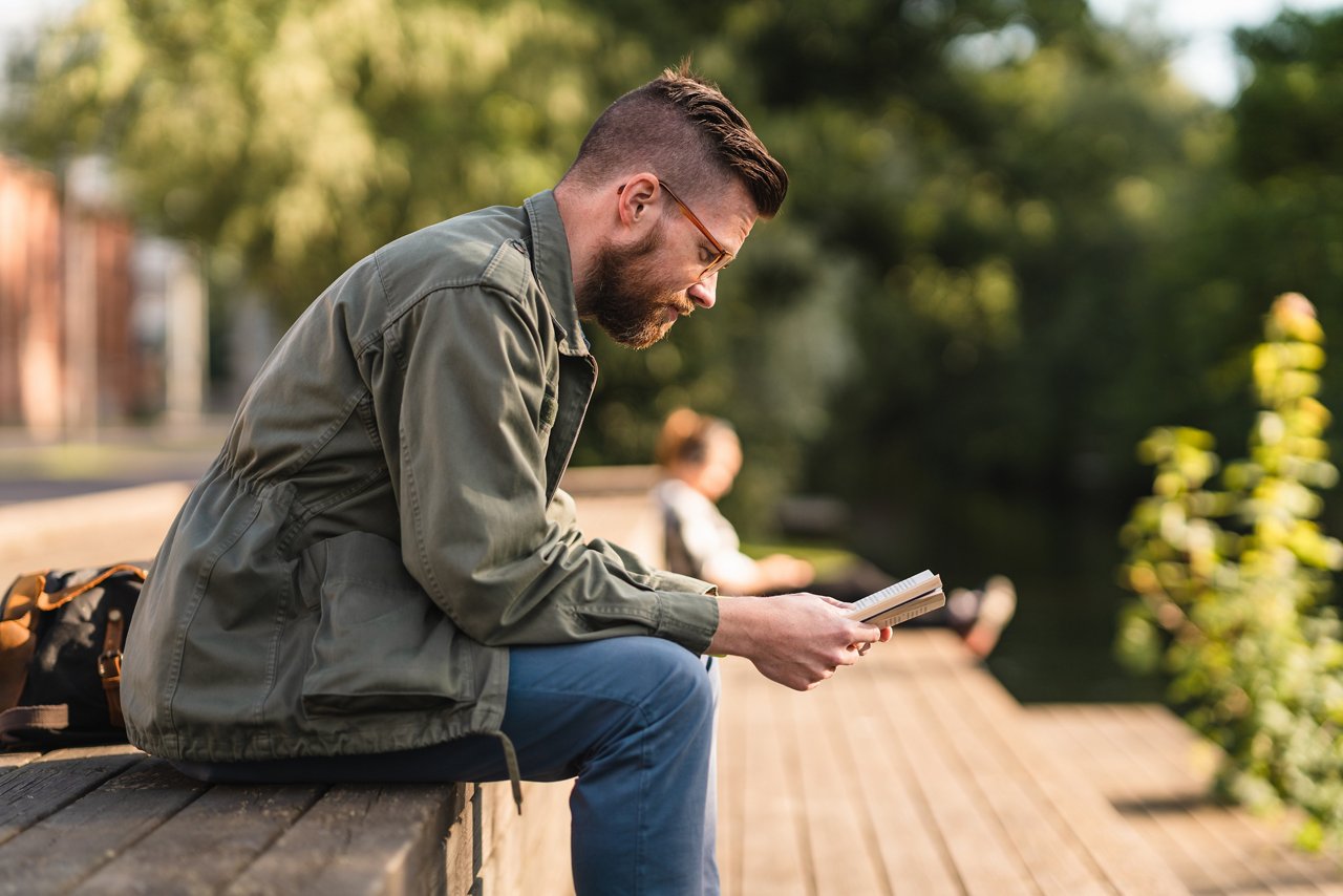 Man reading a paperback book in a public park