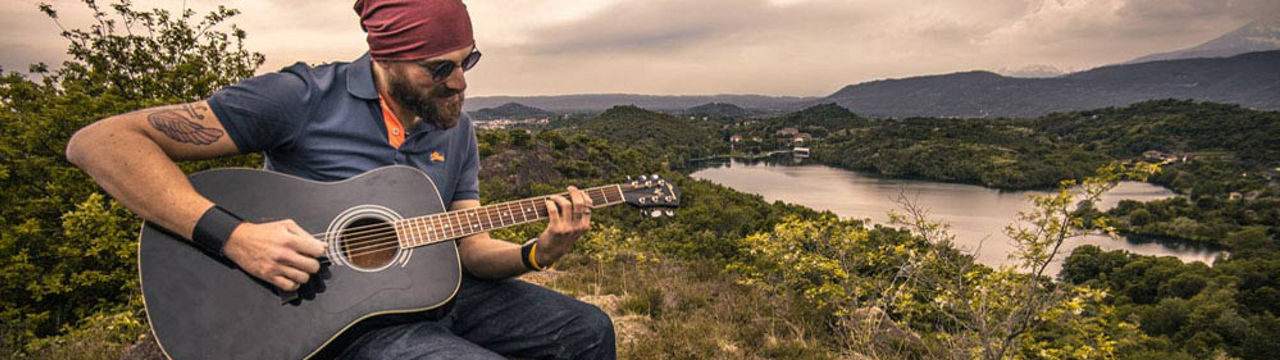 Male playing guitar atop hill overlooking valley