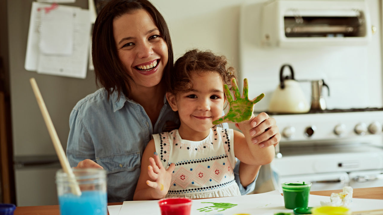 Portrait of mother and daughter painting together in kitchen